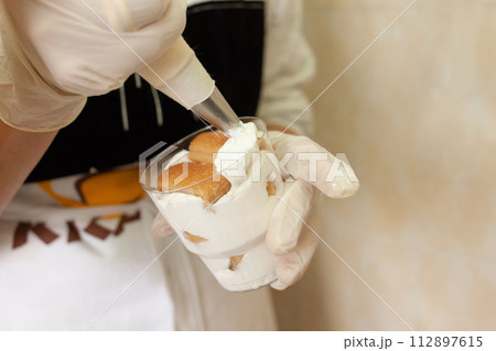 The pastry chef decorates the tiramisu in a glass with whipped cream. 112897615