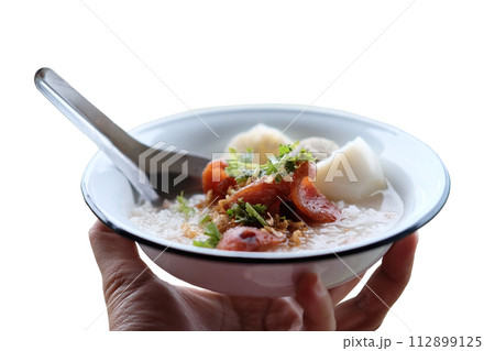 Woman hand holding rice porridge with pork and Fried Chinese sausage in white bowl isolated on white background 112899125