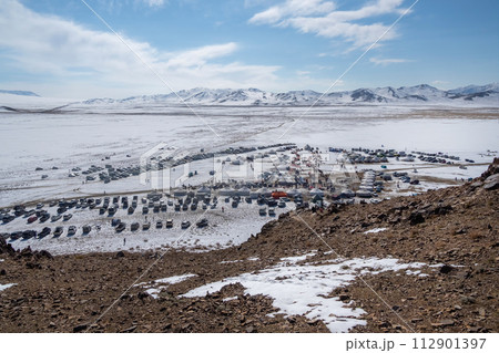 Cluster of tourists, cars and yurts on a sunny snow-covered slope 112901397