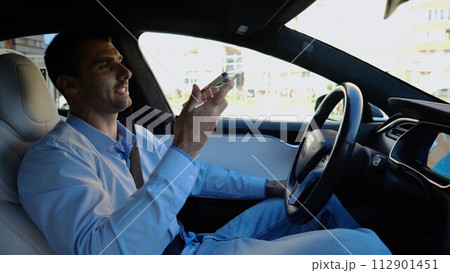 Male businessperson have serious telephone conversation while riding an autonomous self driving electric car. Nervous businessman talks by smartphone during riding on electrical auto with autopilot 112901451