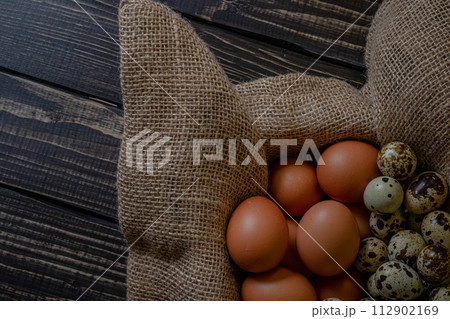 Fresh chicken and quail eggs in a basket on a sack, wooden table.Selective focus Fresh chicken and quail eggs in a basket on a sack, wooden table.Selective focus 112902169