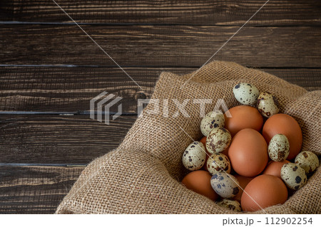 Fresh chicken and quail eggs in a basket on a sack, wooden table.Selective focus Fresh chicken and quail eggs in a basket on a sack, wooden table.Selective focus 112902254