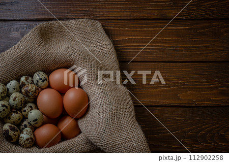 Fresh chicken and quail eggs in a basket on a sack, wooden table.Selective focus Fresh chicken and quail eggs in a basket on a sack, wooden table.Selective focus 112902258