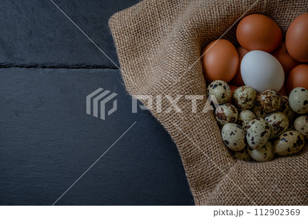 Fresh chicken and quail eggs in a basket on a sack, wooden table.Selective focus Fresh chicken and quail eggs in a basket on a sack, wooden table.Selective focus 112902369