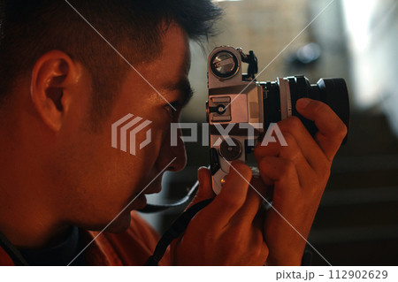 Side view of concentrated photographer looking through viewfinder of camera 112902629