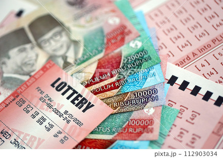 Red lottery ticket lies on pink gambling sheets with indonesian rupiah money bills. Lottery playing concept or gambling addiction in indonesia 112903034