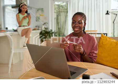 Smiling Black girl filing nails when watching show on laptop at home Smiling Black girl filing nails when watching show on laptop at home 112903244