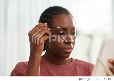 Black teenage girl brushing eyebrows and applying fixing gel 112903246