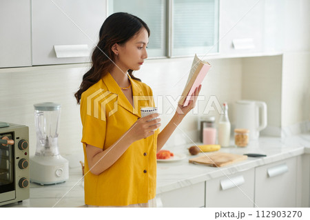 Serious young Vietnamese woman drinking morning coffee and reading book Serious young Vietnamese woman drinking morning coffee and reading book 112903270
