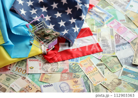 Toy tank on US flag and ukrainian flag on many banknotes of different currency. Background of war funding and military support between United States and Ukraine Toy tank on US flag and ukrainian flag on many banknotes of different currency. Background of war funding and military support between United States and Ukraine 112903363