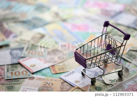 Supermarket trolley on many banknotes of different currency. Background of shopping worldwide close up Supermarket trolley on many banknotes of different currency. Background of shopping worldwide close up 112903371