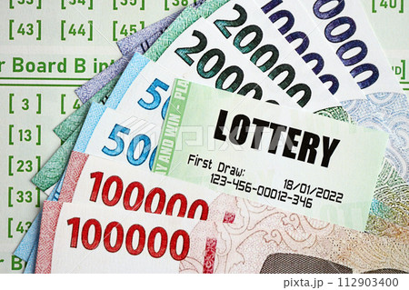 Green lottery tickets and indonesian money bills on blank with numbers for playing lottery close up 112903400