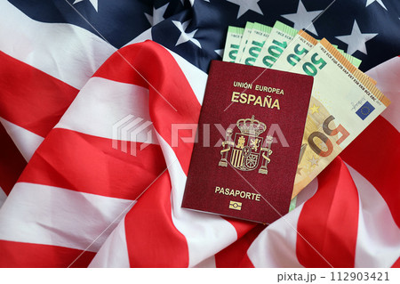 Red Spanish passport of European Union and money on United States national flag background close up. Tourism and diplomacy concept 112903421