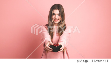Happy female model giving gift box against pink background Happy female model giving gift box against pink background 112904451