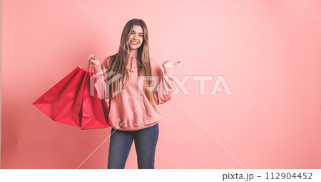 Smiling woman with shopping bags standing against pink background 112904452