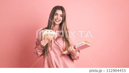 Happy young female student displaying scholarship money with book in pink Happy young female student displaying scholarship money with book in pink 112904453