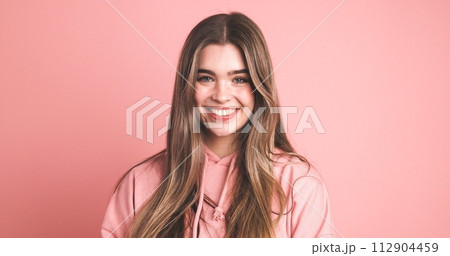 Happy female model in pink hoodie smiling over pink background 112904459