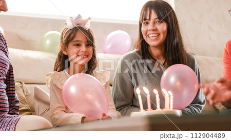 Girl blowing out the candles on her birthday cake sitting on a sofa Girl blowing out the candles on her birthday cake sitting on a sofa 112904489
