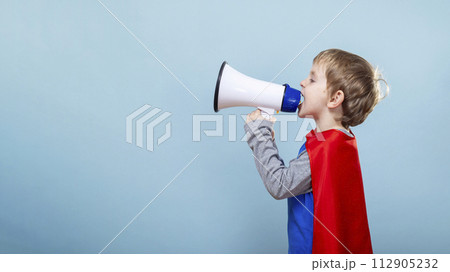 Child in superhero costume using megaphone. Blue background with copy space 112905232