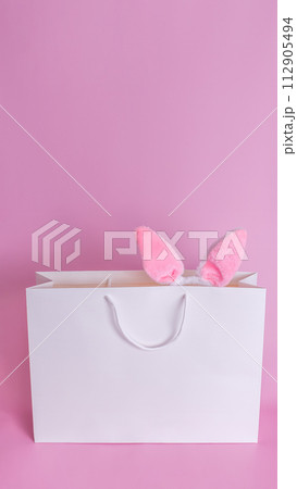 Easter bunny ears in a white paper bag on a pink background. 112905494