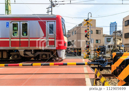 踏切の遮断機と踏切を通過する通勤電車の写真素材 [112905699] - PIXTA