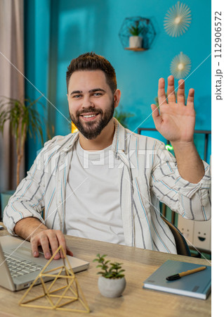 Caucasian young freelancer man smiling at camera waving hands gesturing hello hi greeting at home Caucasian young freelancer man smiling at camera waving hands gesturing hello hi greeting at home 112906572