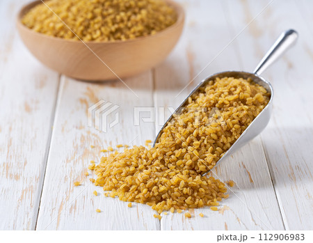 Organic dry bulgur in a metal scoop on a white wooden table. Organic dry bulgur in a metal scoop on a white wooden table. 112906983