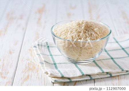 Raw long rice basmati in a glass plate on a white wooden table. 112907000