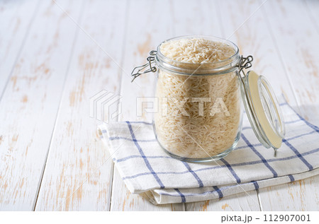 Raw long rice basmati in glass storage jar on a white wooden table. 112907001