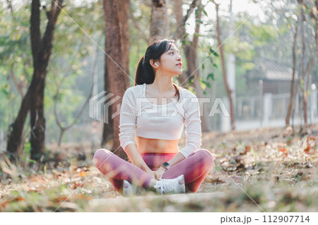 Woman sitting cross legged in a park, looking up thoughtfully after a refreshing outdoor workout session. Woman sitting cross legged in a park, looking up thoughtfully after a refreshing outdoor workout session. 112907714