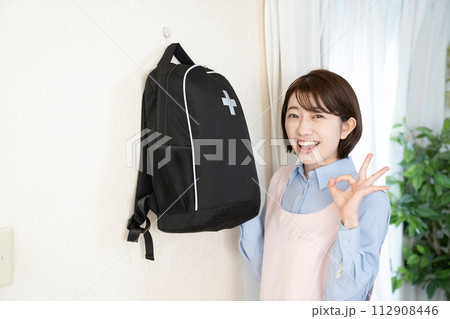 壁に掛けた非常持ち出し袋を持つ女性 112908446