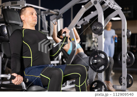 Adult man doing triceps curls in exercise machine in gym 112909540
