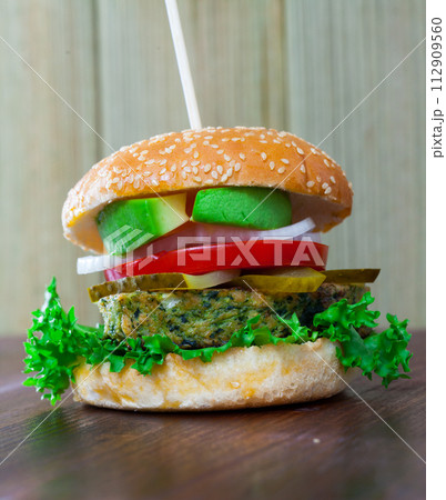 Vegetarian hamburger with soybean patty, fresh vegetables and avocado at plate Vegetarian hamburger with soybean patty, fresh vegetables and avocado at plate 112909560