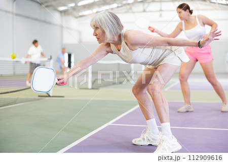 Positive elderly woman playing pickleball on indoor court 112909616