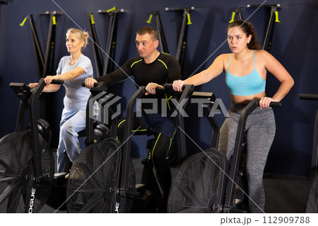 Group of people engaged in a spin bike simulator in the gym, exercising on stationary bike Group of people engaged in a spin bike simulator in the gym, exercising on stationary bike 112909788