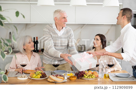 Birthday senior man accepts outright gift and greetings from adult son during family feast Birthday senior man accepts outright gift and greetings from adult son during family feast 112909899