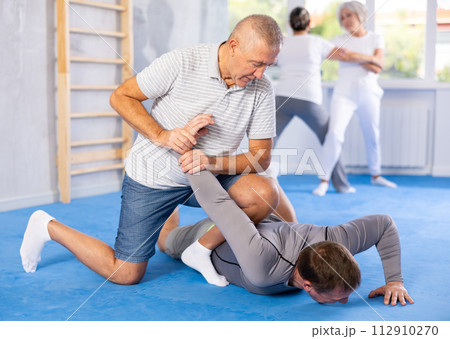 Old man twisting her opponent's arm during self-defense classes 112910270