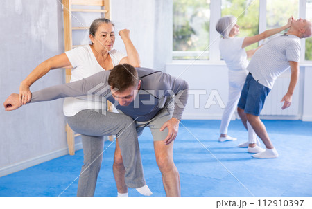 Senior woman in pair with middle-aged coach train Krav Maga and self-defense skills. 112910397
