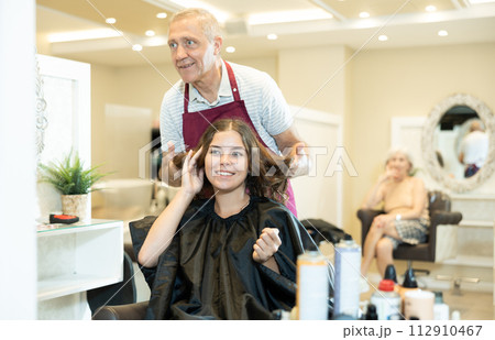 Experienced man hairdresser discussing hairstyling with young female client 112910467