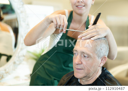 Senior gray-haired male client getting haircut in hairdressing salon Senior gray-haired male client getting haircut in hairdressing salon 112910487