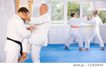 Old man attendee of karate classes fighting with his opponent in sports hall Old man attendee of karate classes fighting with his opponent in sports hall 112910543