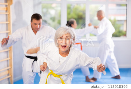 Mature women and men in pairs exercising karate movements during group training 112910593