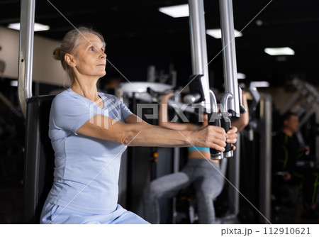 Portrait of elderly woman during workout with power exercise machine in gym Portrait of elderly woman during workout with power exercise machine in gym 112910621