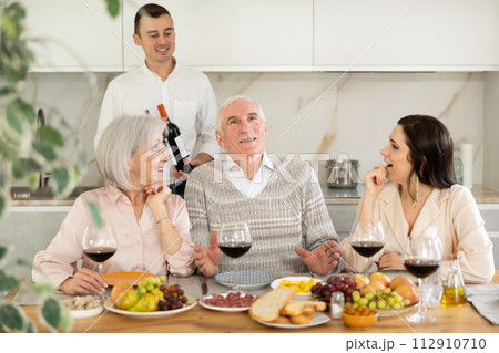 Senior parents and young couple sitting at table drinking wine and having conversation Senior parents and young couple sitting at table drinking wine and having conversation 112910710
