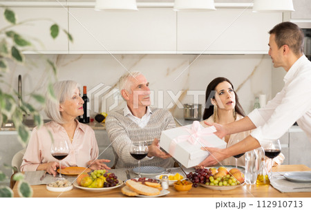 Caring son-in-law surprising father-in-law with present during family feast Caring son-in-law surprising father-in-law with present during family feast 112910713