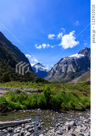 夏の晴れた日のミルフォードサウンド近くの小さい川と雪山と青空 112912010