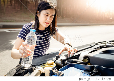 Asian woman check the radiator system and fluid level in the car radiator is too low after engine overheated,she uses water instead of coolant while traveling,outdoor emergency on the side of the road Asian woman check the radiator system and fluid level in the car radiator is too low after engine overheated,she uses water instead of coolant while traveling,outdoor emergency on the side of the road 112915886