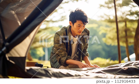キャンプ場でテントを設営する日本人男性 112916433