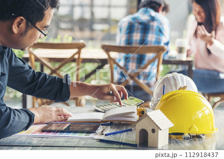 Civil construction engineer working with laptop at desk office with white yellow safety hard hat at office on construction site. Asian young man architecture project manager sitting at office on site Civil construction engineer working with laptop at desk office with white yellow safety hard hat at office on construction site. Asian young man architecture project manager sitting at office on site 112918437