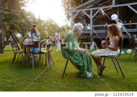 Girl playing on guitar for her grandmother at garden party. Love and closeness between grandparent and grandchild. 112919524